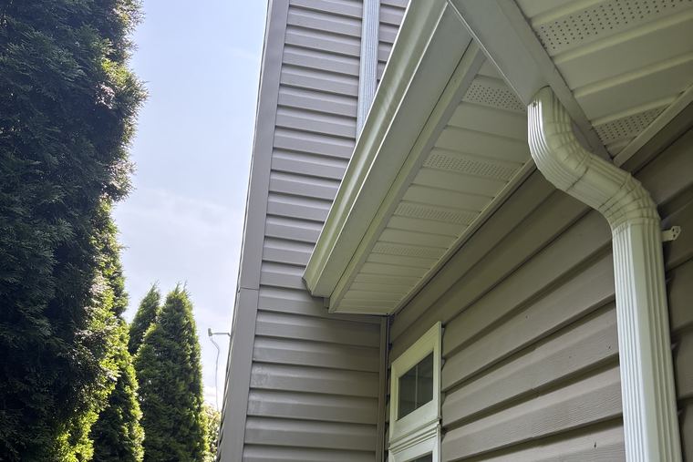 White gutter, downspout and soffit cleaned and brightened against a blue sky