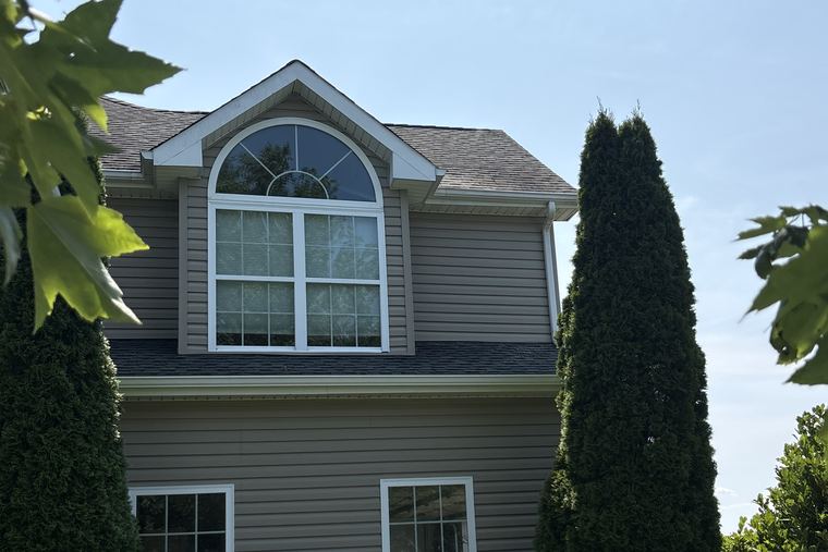 Two-storey home with tan siding and a shingle roof, clean after house soft washing