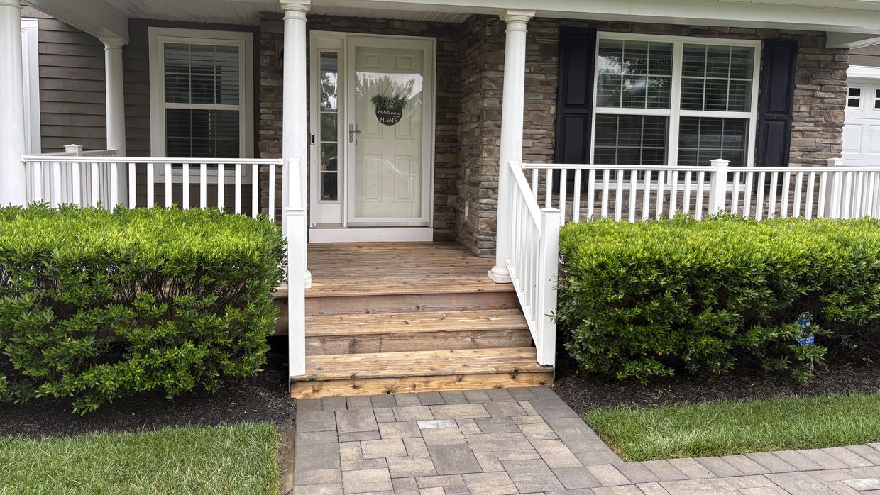 A cleaned front porch with stone facing, white railings and clean paver walkway